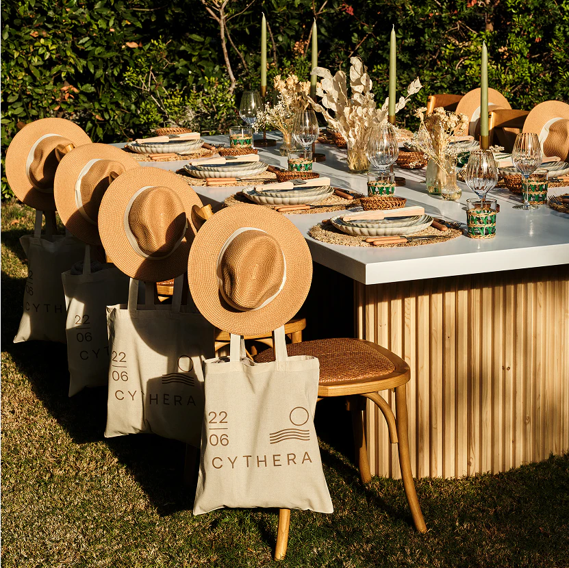 Elegant outdoor event table setup with customized tote bags and straw hats as guest gifts.